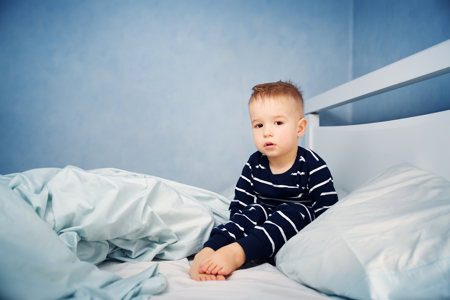 Sleepy boy sitting in bed. Tired child in bedroom