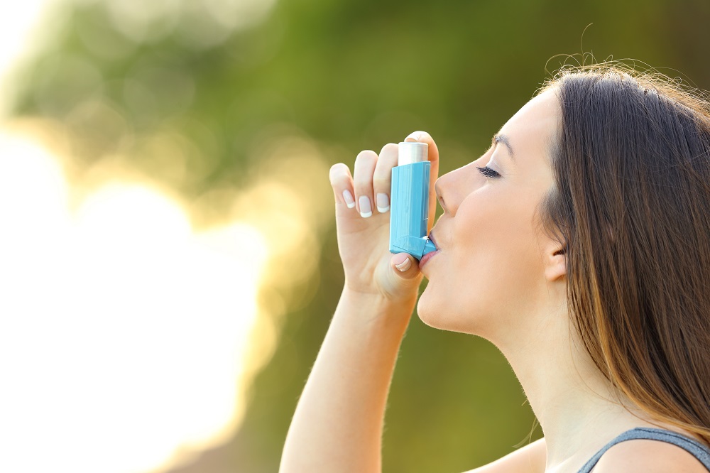 Side view of a woman using an asthma inhaler outdoors with a green background