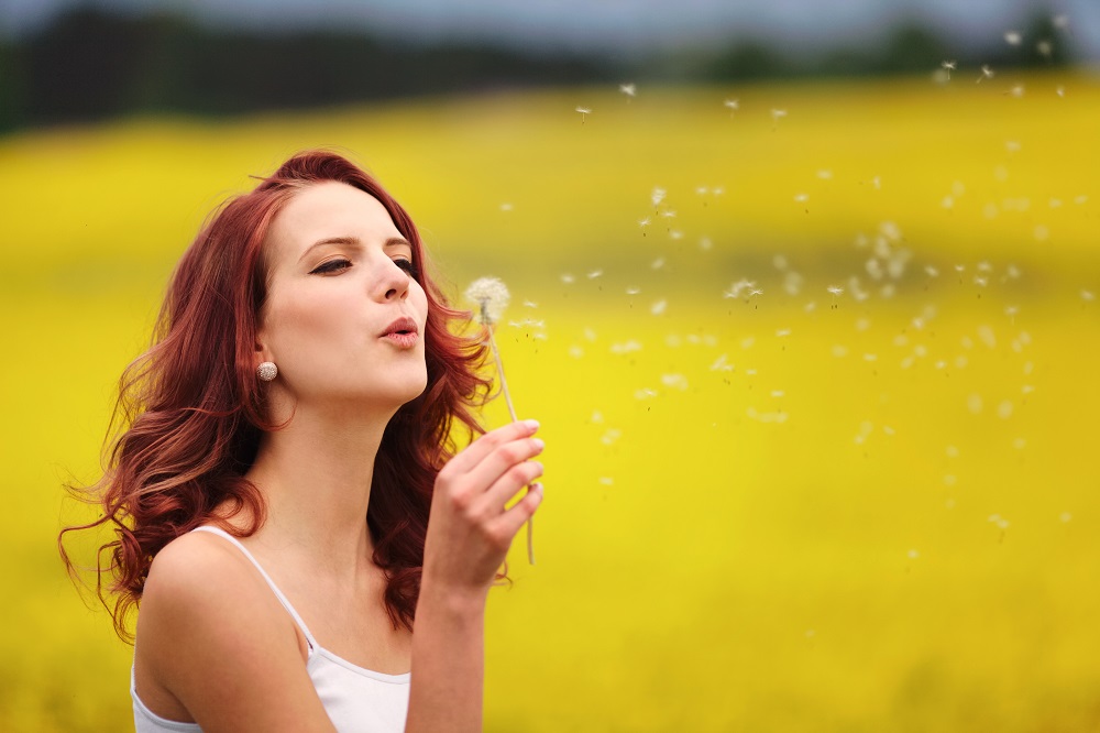 happy beautiful woman blowing dandelion in the field